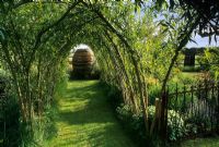 Living willow tunnel with grass path. Woven willow vessel at end. Side exit though to main garden with iron gate - Suffolk 