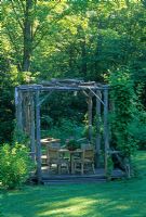 Table and chairs on shaded deck patio  beneath wooden arbour made with rustic poles - NY State, USA 