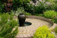 Round paved area with water feature based on a dark coloured urn