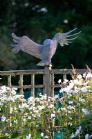 Owl sculpture made of wire netting, wooden lichen-covered fence and Japanese Anemone-Anemone x hybrida 'Honorine Jobert'