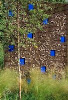 Dividing wall of gabions filled with pebbles punctuated with blue glass plates - Westonbirt Garden Festival  