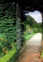 Brick path leading through metal gate in hedge divider to separate garden. With gravel path, low Buxus hedge and border - Cloudehill, Olinda, Victoria, Australia