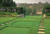 Paving slabs in lawn leading to gap in hedge and view beyond. Sunken squares in lawn. Borders of Agapanthus infront of hedges - Garangula, Harden, NSW Australia