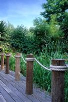 Decked boardwalk with posts and rope swags in sub-tropical urban garden. Planting of Cordyline and reeds - Drybrugh Road London 
