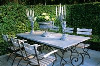 Dining table and chairs on terrace behind hedges 