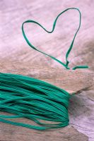 Green plastic coated tie wire twisted in to heart shape on wooden table