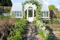 Greenhouse in spring potager with step-over espaliered apples and brick path