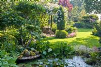 Pond in country garden with reclining sculpture on wooden decking