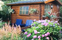 Two seats in front of log cabin decorated with hanging plants