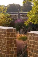 View through stone wall into dry garden with Stipa arundinacea, Verbena bonariensis and driftwood sculpture in background