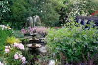 Garden pond with fountain - Plants include Rosa 'Grussan Achen', Iris pseudacorus 'Yellow Flag' and Saxifraga x urbium