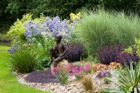 Summer border with statue 'Boy on the Rock' by Jane Hogben set on a boulder in a gravel bed