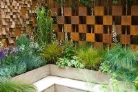 Mixed grasses and perennials surround a sunken seating area with a backdrop of walls created from corten steel boxes and irregular wooden blocks - Garden - The Pemberton Greenish Recess Garden, Designer - Paul Hensey with Knoll Gardens, Sponsor - Pemberton Greenish