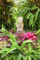 Stone statue in tropical garden amongst  Bromeliad and Boston Fern