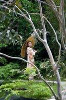 Japanese lady in traditional dress with parasol through branches of Eucalyptus. Garden in the Silver Moonlight, Design Haruko Seki and Makoto Saito. Sponsor - Royal Palm Residences Seychelles, Urban Regenerate Association of Niigata Supported by - The Great Britain Sasakawa Foundation, The Japan Society
