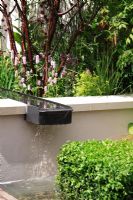 A water rill leading from a pool and sunken seating area in a courtyard garden surrounded by planting of mixed perennials, shubs, herbs and grasses in the A Welcome Sight Garden, Designed by Adam Frost, Chelsea Flower Show 2008, Best Urban Garden Gold medal Winner