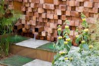 Wooden block wall with water spouts. Plants include Artemisia 'Powis Castle', Phlomis russeliana and Cyperus papyrus. The Pemberton Greenish Recess Garden, Design - Paul Hensey
