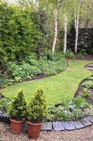 Simple ovoid shaped lawn in well tended garden in Spring with Victorian tiles as decoration