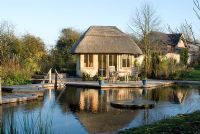 Natural swimming with thatched timber pool house surrounded by decking in November