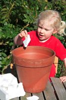Young child girl putting polystyrene pieces in terracotta pot for drainage