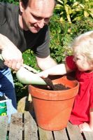 Young child girl and man putting compost in terracotta pot 