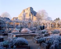 Frozen pond creates a focal point for the herb garden with frosted wigwams, the circular arcaded walk and ruined abbey in the background - The Abbey House, Wiltshire