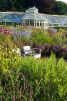 Glasshouse and wooden seats in The Walled Garden planted with Origanum 'Rosenkuppel', Perovskia 'Blue Spire', Phlomis russeliana and Amsonia - Scampston Hall, Yorkshire designed by Piet Oudolf