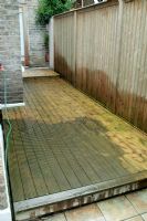 Area of decking down the side of a terraced town house in the process of being cleaned using a pressure washer.