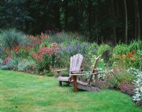 Seping border beside wooden adirondack chairs with Echinacea, Nepeta and ornamental grasses - Greystone Cottage, Oxfordshire