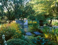 Morning light on the lily pond with decking, adirondack chairs, stepping stones, concrete sculpture and Rudbeckia deamii - Greystone Cottage, Oxfordshire