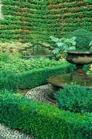 Small formal garden with water feature, espaliered Pyrcantha and seat - Bourton House, Gloucestershire
