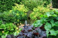 Stone water feature with Euphorbia stygiana, Euphorbia mellifera and Primula hybrids - Hunmanby Grange, Yorkshire