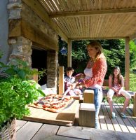 Woman cooking homemade pizza in outside pizza oven in garden with hungry children waiting in background - Devon
