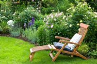 Wooden reclining chair next to flowerbed with Rosa 'Mary Rose' and Rosa 'The Pilgrim'