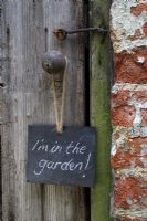 Slate sign hanging on rustic door, reading 'I'm in the garden'