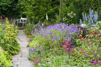 Mixed summer border of Delphiniums, Phlomis russeliana, Nepeta 'Walker's Low', Geranium 'Johnson's Blue and Centranthus ruber leading to seating area