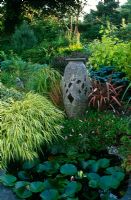 Stone urn beside small pond with Phormium, Hakonechloa, Persicaria affinis and Nymphaea - Lakemount, Glanmie, Cork, Republic of Ireland