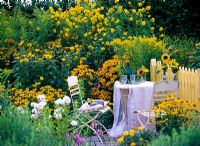 Seating area surrounded by hot bed of Rudbeckia 'Goldsturm' 'Goldball', Helianthus decapetalus 'Capenoch Star' and Solidago 