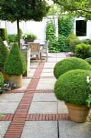 Brick and stone paved patio with wooden dining table and chairs and clipped Buxus topiary