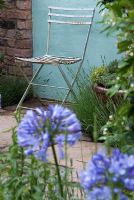 Chair on stone patio with herbs in the The Scented Walled Garden and Agapanthus in foreground, Exhibitor - Arley Hall at RHS Tatton Flower Show 2008