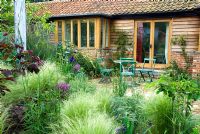 Terrace with seating area, mixed border includes Stipa tenuissima, Allium, Iris and Cercis canandensis 'Forest Pansy'