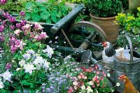 Mixed flowerbed with ornamental wooden wheelbarrow and galvanised watering can