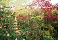 Acers, Camellias and Rhododendrons surrounding a decorative stone pagoda - The Japanese Garden, St Mawgan, Cornwall
