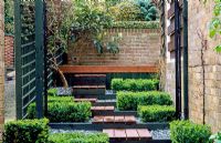 Decked steps with slate mulched beds and 
Box cubes, Buxus sempervirens 'Suffruticosa'. Large shrub against the back wall is Eriobotrya japonica