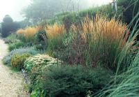 Double herbaceous border with Calamagrostis 'Karl Foerster', Sedum sepctabile 'Autumn Joy', catmint, tradescantia and Asters with their twiggy supports at Kingston Maurward Gardens