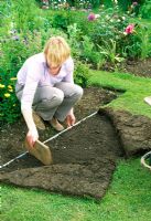 Woman leveling lawn by peeling back turf and adding more soil