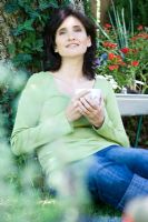 Woman leaning against tree in garden having a teabreak