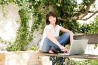 Woman sitting on table in the garden using laptop computer