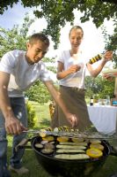 Couple cooking vegetable kebabs on barbecue in garden