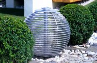 A spherical water feature with balls of clipped Buxus topiary in 'The Winalot Live a Lot' garden designed by Chris Beardshaw at RHS Hampton Court Flower Show